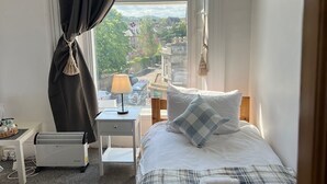 A bedroom with a bed, a bedside table, a lamp, a heater, and a view of the city. - Edinburgh Travel Guest House (Edinburgh)