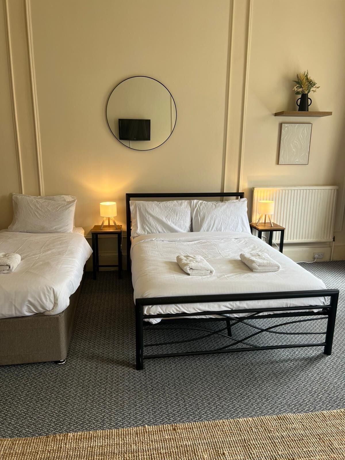 A hotel room with a bed, two bedside tables, a TV, and a radiator.