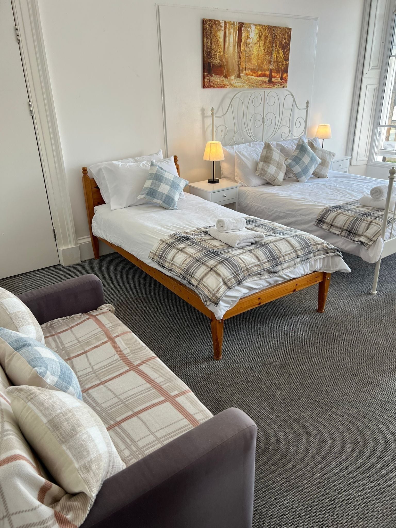A hotel room with two single beds, a sofa, and a painting on the wall.