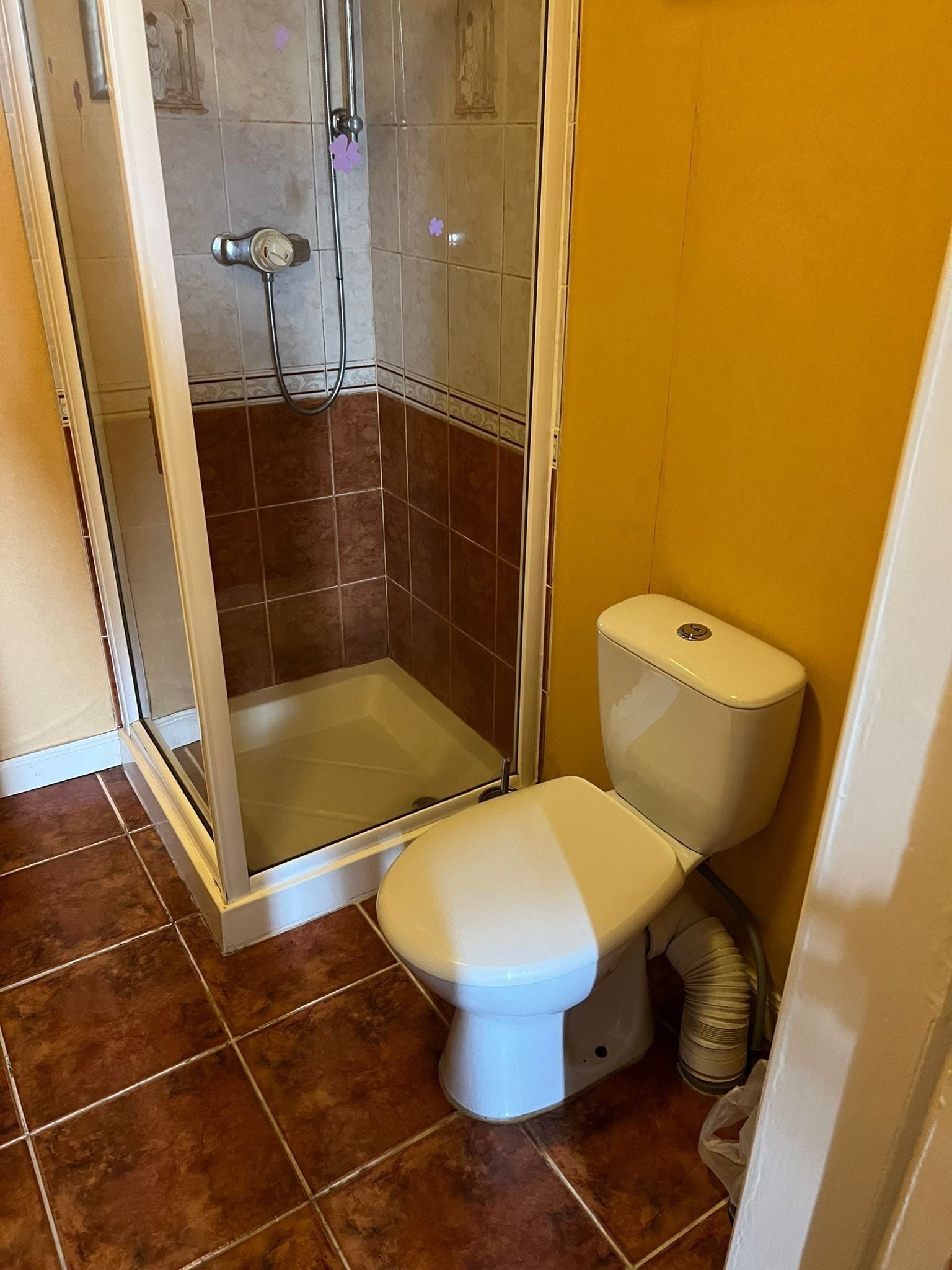 Un baño pequeño con ducha, inodoro y suelo de baldosas.