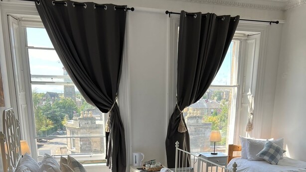 A hotel room with two beds, black curtains, a view of the city, and a small table with a lamp. - Edinburgh Travel Guest House (Edinburgh)