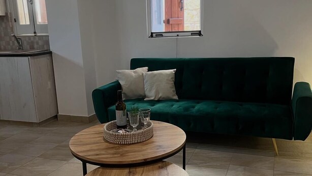 Un espacio de estar con un sofá verde, una mesa de centro redonda de madera y una ventana con vista a una puerta roja.