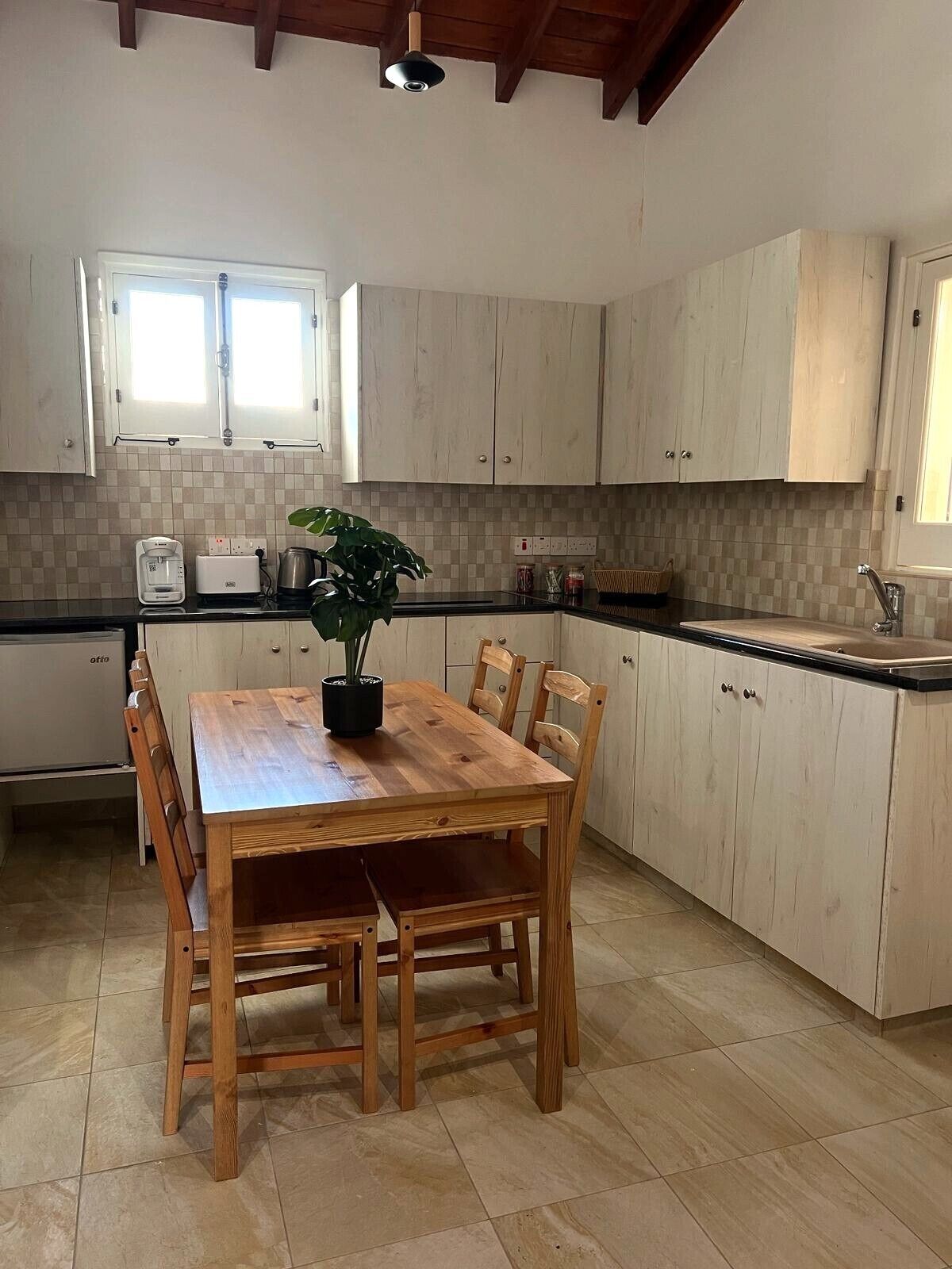 A kitchen with a wooden table and chairs, light-colored cabinets, and a tiled backsplash.