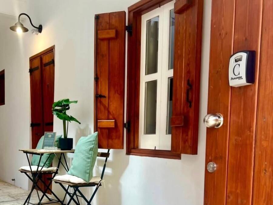 A room with a wooden door, a window with shutters, a small table with chairs, and a potted plant.