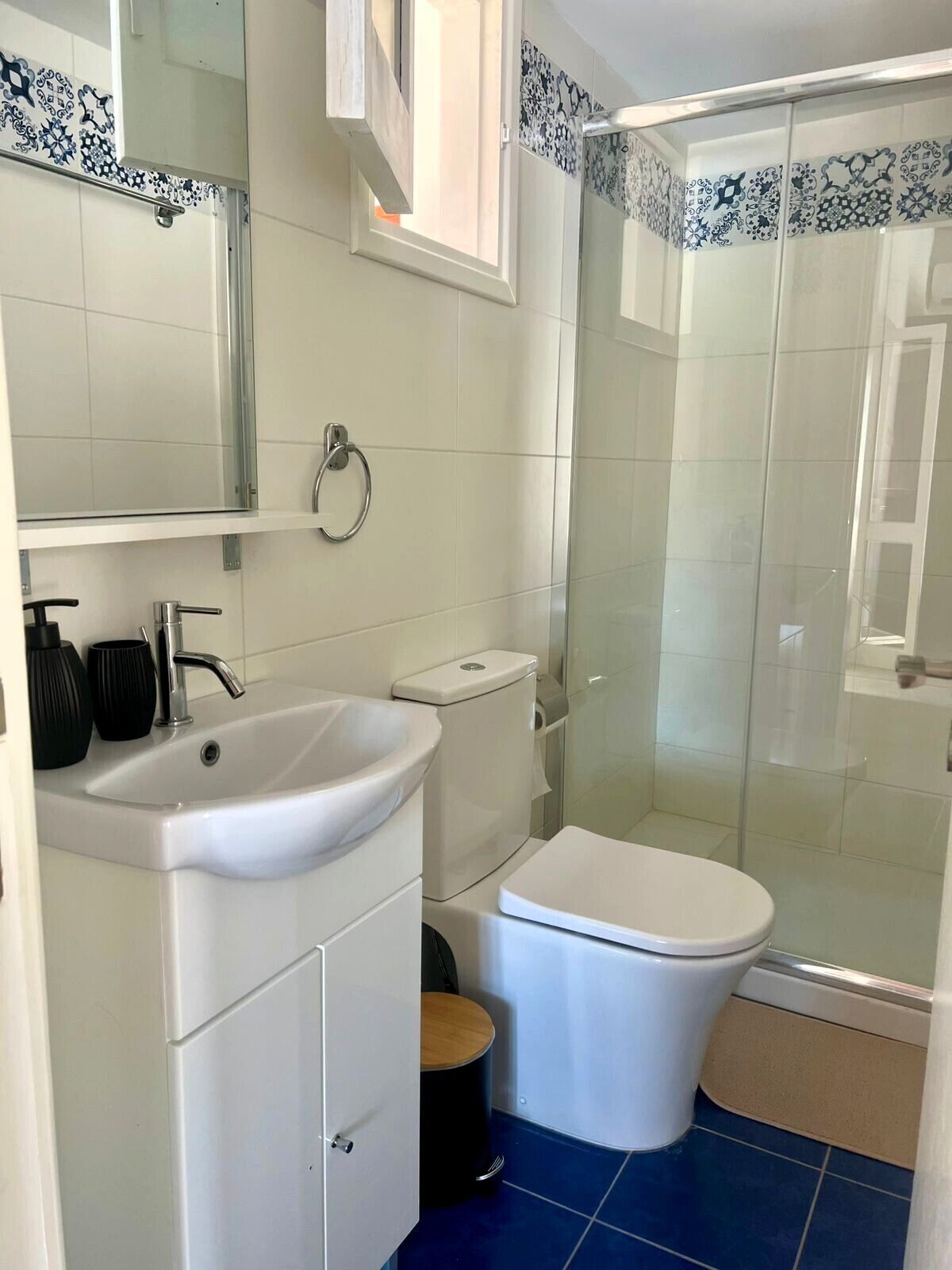 A modern bathroom with a white sink, toilet, and glass shower enclosure.