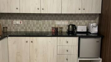 Una cocina con armarios de madera clara, salpicadero azulejado, cafetera, tostadora y refrigerador pequeño.