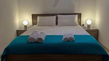 Ein ordentlich bezogenes Bett mit zwei aufgerollten Handtüchern, einem hölzernen Kopfteil und zwei Nachttischlampen.