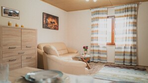 A cozy living room with a sofa, a small table with candles, and a window with striped curtains.