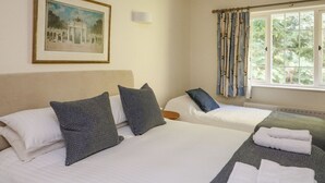 Habitación de hotel con dos camas, un cuadro enmarcado en la pared, una ventana con cortinas y vistas al exterior con vegetación.