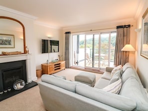 A living room with a fireplace, a sofa, a TV, and a balcony with outdoor seating. - 4 St Elmo Court DO NOT USE (Salcombe)