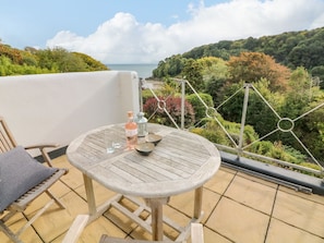 A round wooden table with a bottle and glasses on a balcony overlooking a forested landscape. - 4 St Elmo Court DO NOT USE (Salcombe)