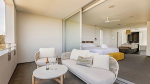 Una camera d'hotel moderna con un balcone, un divano, un piccolo tavolino con una bottiglia e un bicchiere, e un letto con testiera e cuscini.
