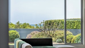 Una stanza con un'ampia finestra che si affaccia su un giardino curato e sull'oceano.