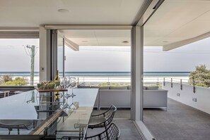 Un espace repas moderne avec une table en verre, des chaises en métal et une vue sur la plage.