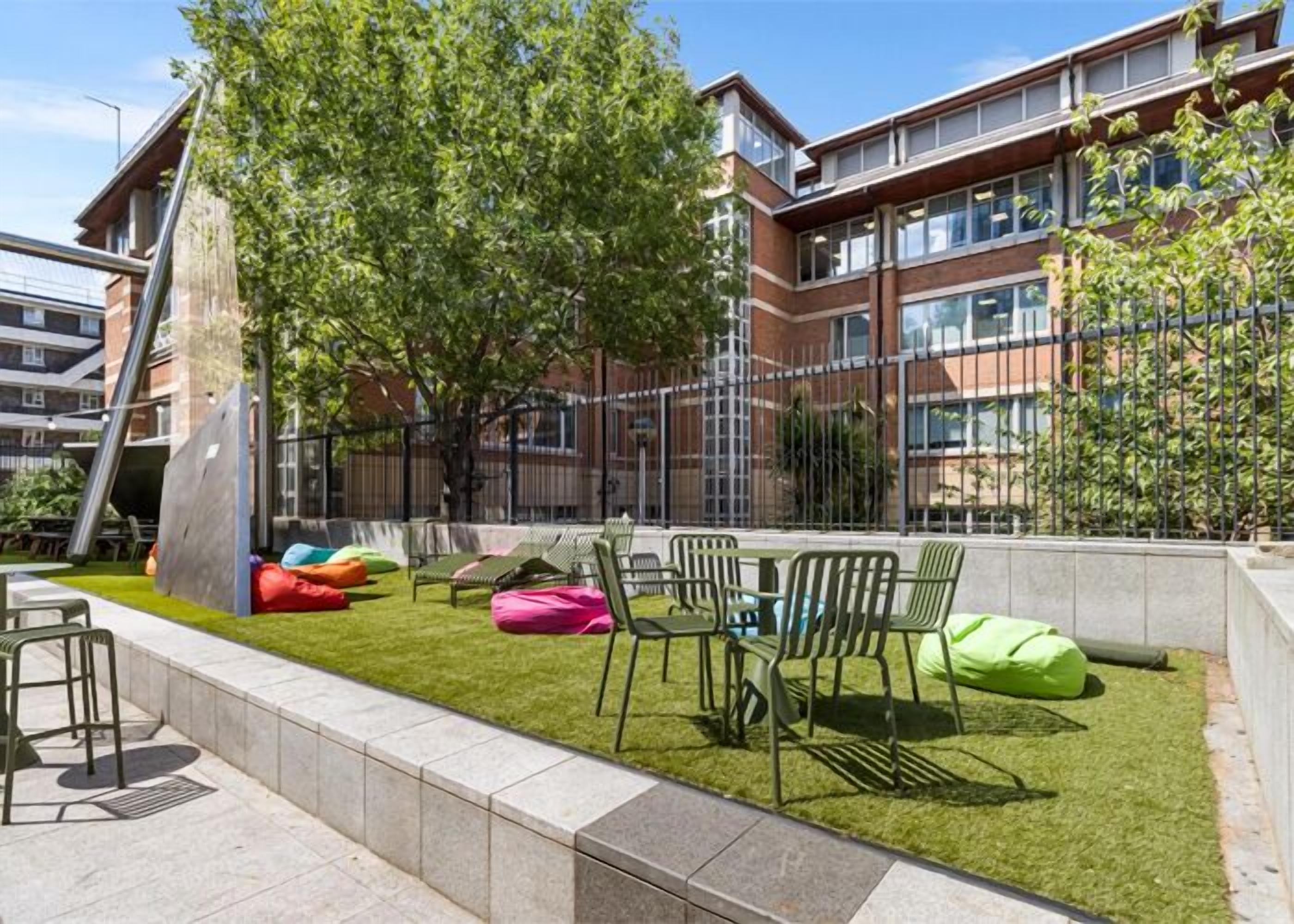 An outdoor seating area with chairs and bean bags, surrounded by a grassy lawn and trees.
