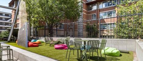 An outdoor seating area with chairs and bean bags, surrounded by a grassy lawn and trees.