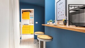 Una cocina con una pared azul de acento, un armario amarillo, dos taburetes y un refrigerador.