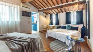 Habitación de hotel con techo de madera, cama con ropa blanca, escritorio con silla y una pequeña mesa redonda con un libro.