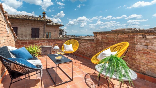Un patio con sillas de mimbre, una mesa y plantas en macetas.