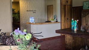 Ein Empfangsbereich mit einem Holzbüro, einem an der Wand befestigten Schild mit der Aufschrift "MANDALAY 1941" und einer Holztür.