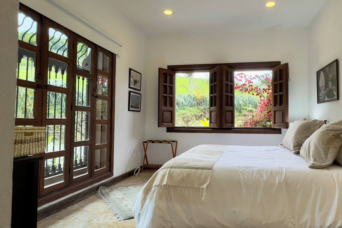 Un dormitorio con una cama grande, una ventana con contraventanas de madera y vistas a la vegetación.
