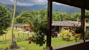 Blick von einer überdachten Veranda auf einen üppigen Garten mit Bergblick.