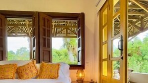 Ein Schlafzimmer mit einem großen Bett, einem Nachttisch und Blick auf Grün hinter geöffneten Türen.