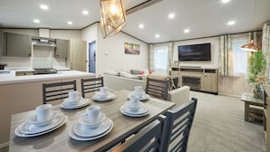 A modern kitchen with a central island, dining area with white tableware, and a living space with a TV and fireplace. - Host & Stay | Happy Day's Lodge (Pocklington)