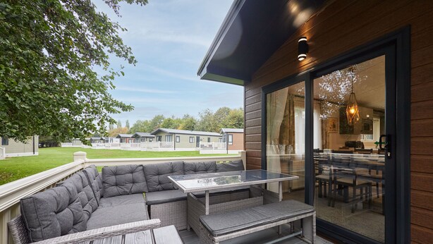 A modern outdoor patio with a sectional sofa, a glass-top table, and a wooden deck. - Host & Stay | Happy Day's Lodge (Pocklington)