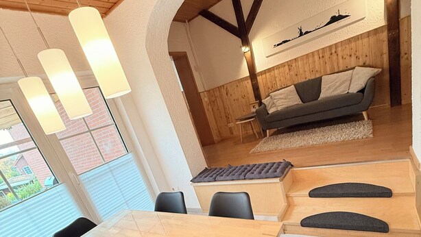 Een moderne eetruimte met een houten tafel en zwarte stoelen, een bank en een aan de muur bevestigd kunstwerk.