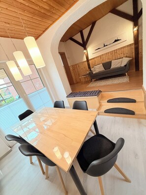 Uma área de refeições moderna com mesa de madeira e cadeiras pretas, um sofá e uma obra de arte pendurada na parede.