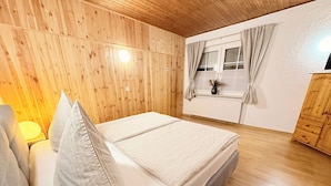 Een kamer met houten lambrisering, een bed, een raam met gordijnen en een radiator.