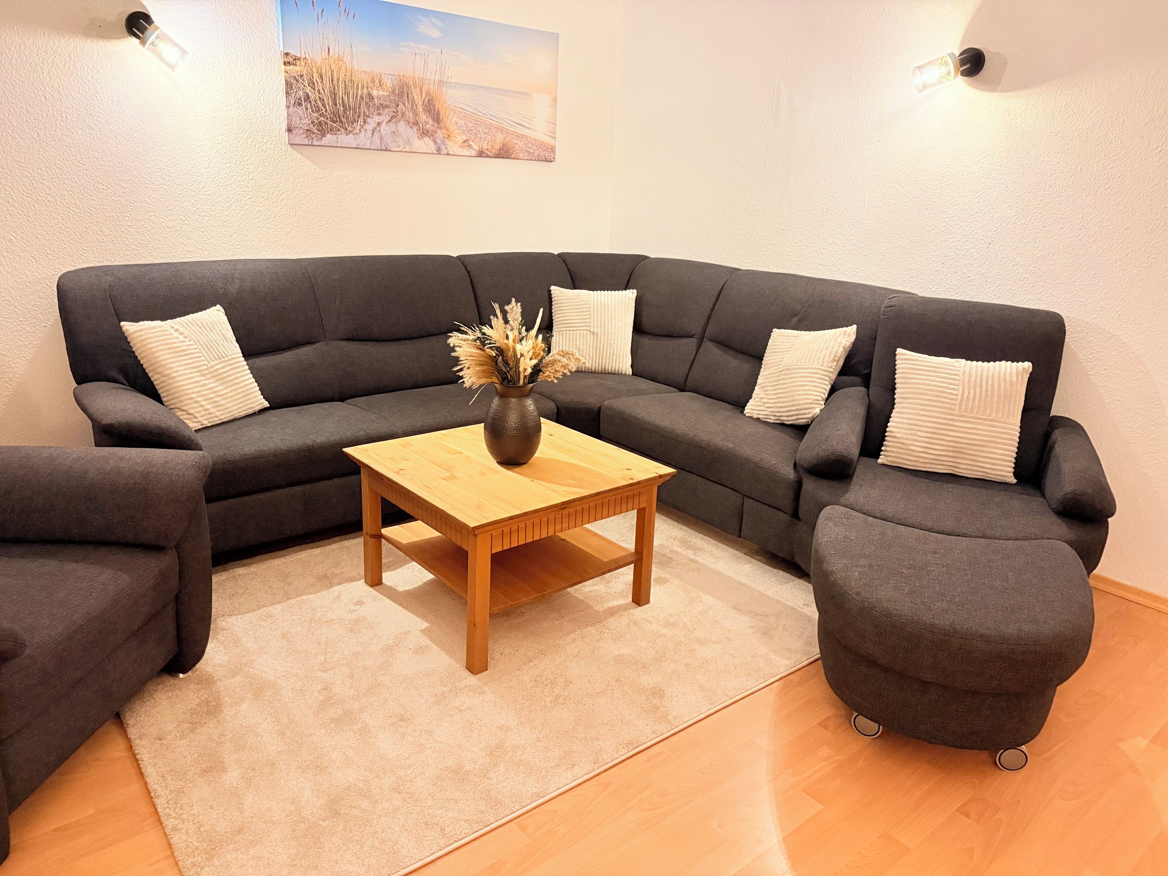 A modern living room with a dark grey sectional sofa, a wooden coffee table, and a vase with dried plants.