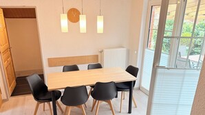 Een moderne eetruimte met een houten tafel en zwarte stoelen, een klok aan de muur en uitzicht op groen buiten.