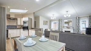 Eine moderne Küche mit eingebauten Geräten, ein Essbereich mit Tisch für vier Personen und ein Wohnbereich mit Sofa und Kamin.