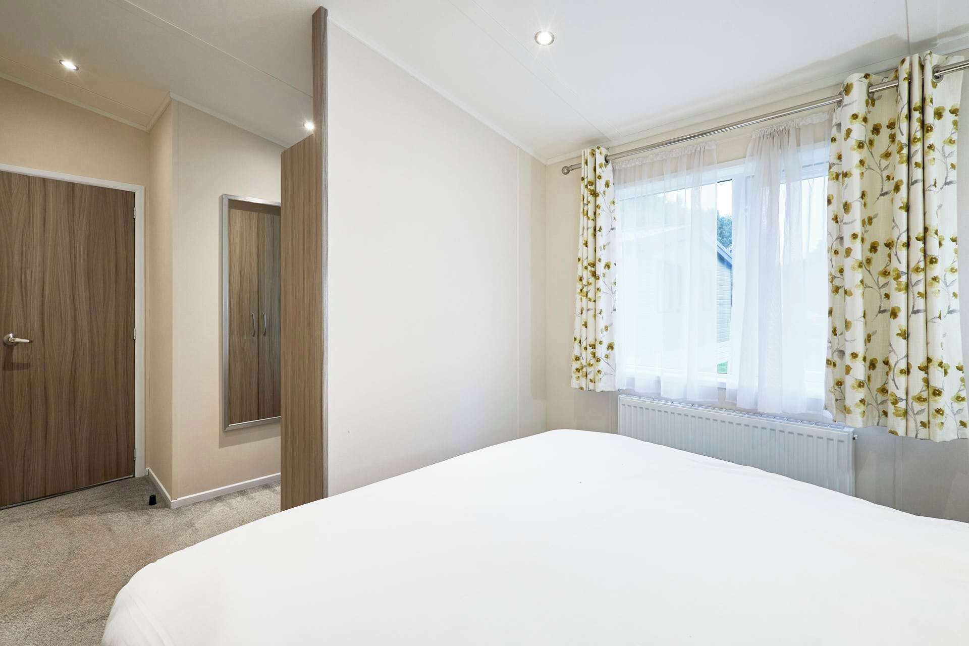 Un dormitorio con una cama grande, un armario, una ventana con cortinas florales y un radiador.