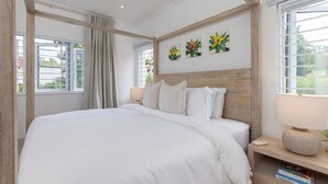 Une chambre avec un grand lit, une tête de lit en bois et trois tableaux représentant des fleurs, accrochés au mur.