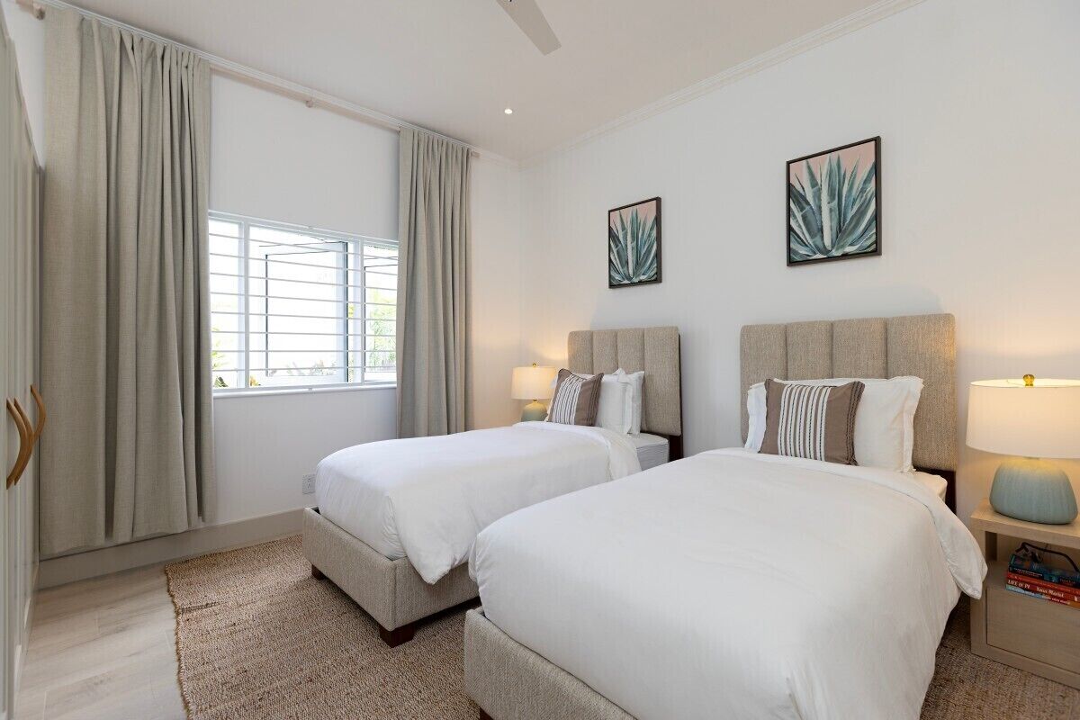 Quarto de hotel com duas camas, uma janela grande com cortinas e duas luminárias fixadas na parede.