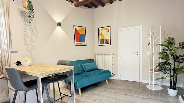 Une pièce avec un plafond en bois, une table à manger avec des chaises, un canapé de couleur turquoise et un radiateur blanc.