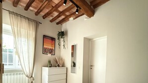 Une chambre avec un plafond en bois, un lit recouvert d’une literie à motifs floraux, une commode et une fenêtre avec des rideaux.