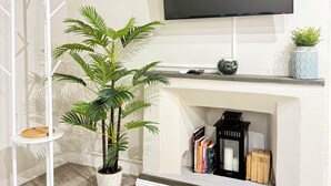 Un salon moderne avec un téléviseur à écran plat fixé au-dessus d’une cheminée, un porte-manteau blanc et une plante en pot.
