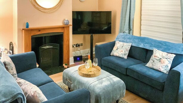 Una sala de estar con chimenea, un televisor de pantalla plana y dos sofás azules con cojines estampados.