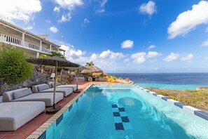 Une piscine offrant une vue dégagée sur l’océan, des chaises longues et un bâtiment doté d’un balcon.