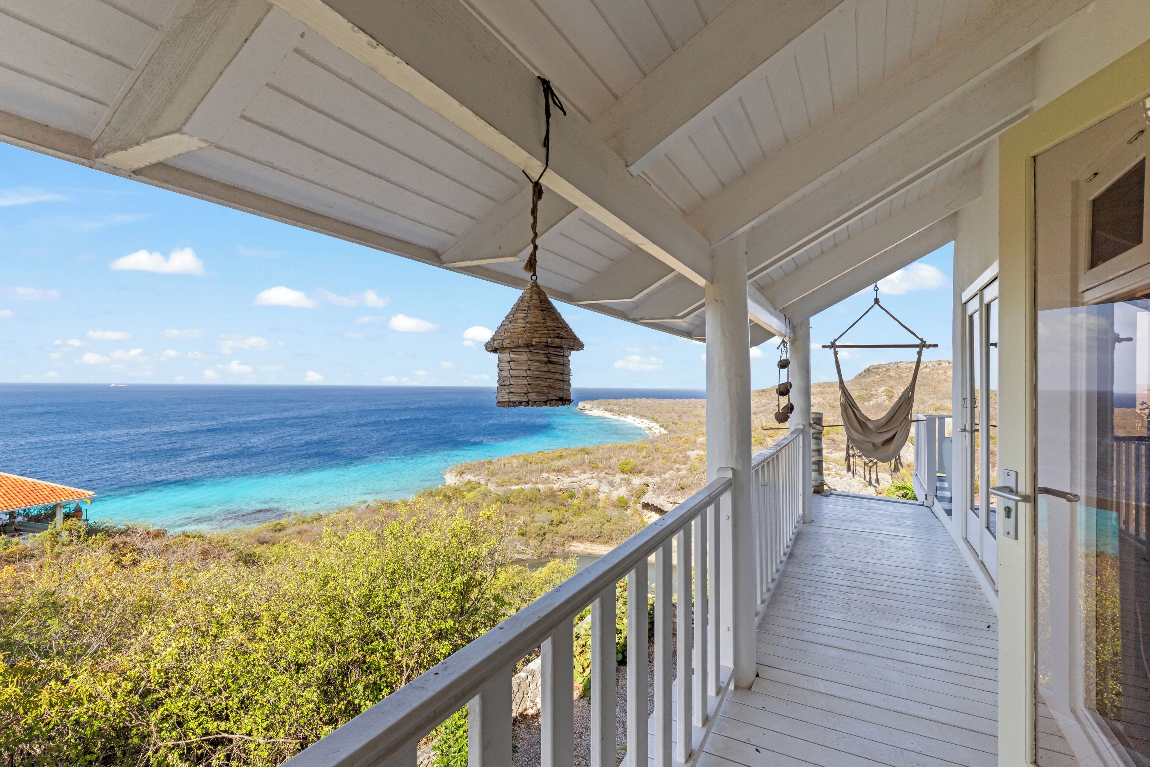 A covered porch with a view of the ocean, a hanging lantern, and a hammock.