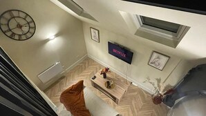 A modern living room with a sofa, a coffee table, a clock, a TV displaying 'NETFLIX', and a fireplace. - Chic Apartment on The Headrow, Leeds (Leeds)