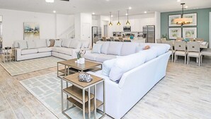 Un salon moderne avec un canapé d’angle, une table basse et un coin repas agrémenté d’un lustre.