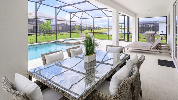 Une terrasse fermée par des baies vitrées, avec une piscine, des meubles en osier et un espace barbecue.