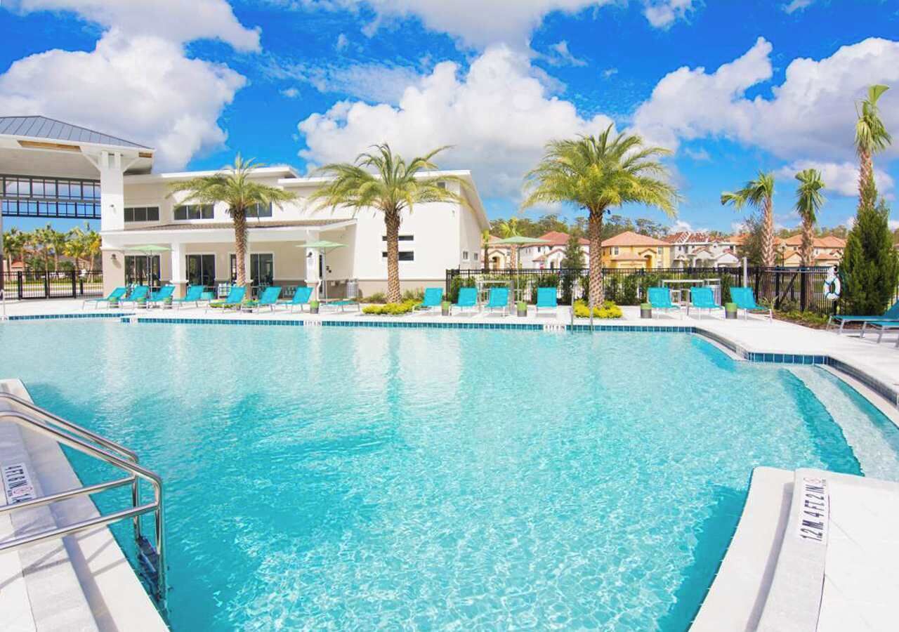 A large outdoor swimming pool with clear blue water, surrounded by lounge chairs and palm trees.