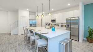 Une cuisine moderne avec des meubles blancs, des appareils en acier inoxydable, un îlot central doté de sièges et des luminaires suspendus.