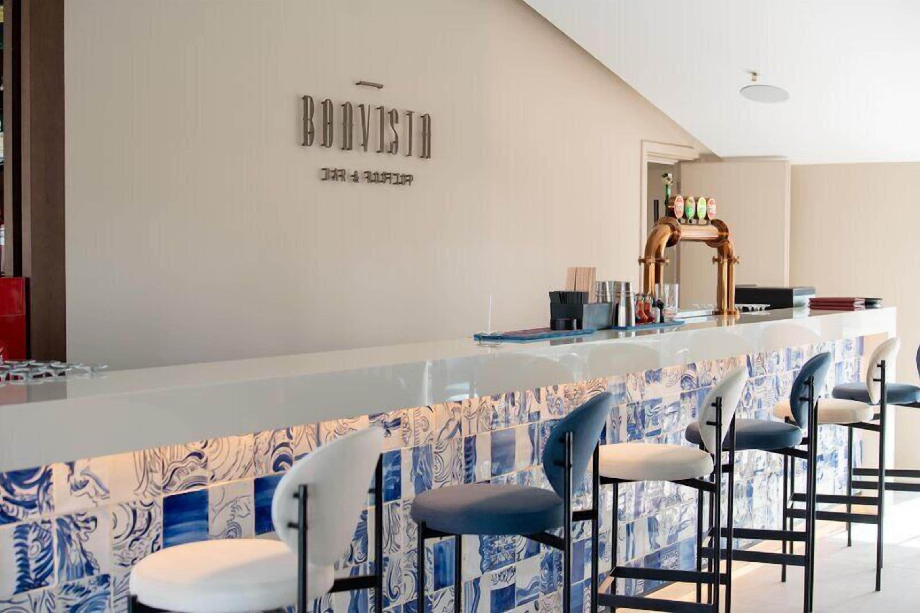 A bar area with a counter and bar stools, a wall with a name sign, and a patterned backsplash.
